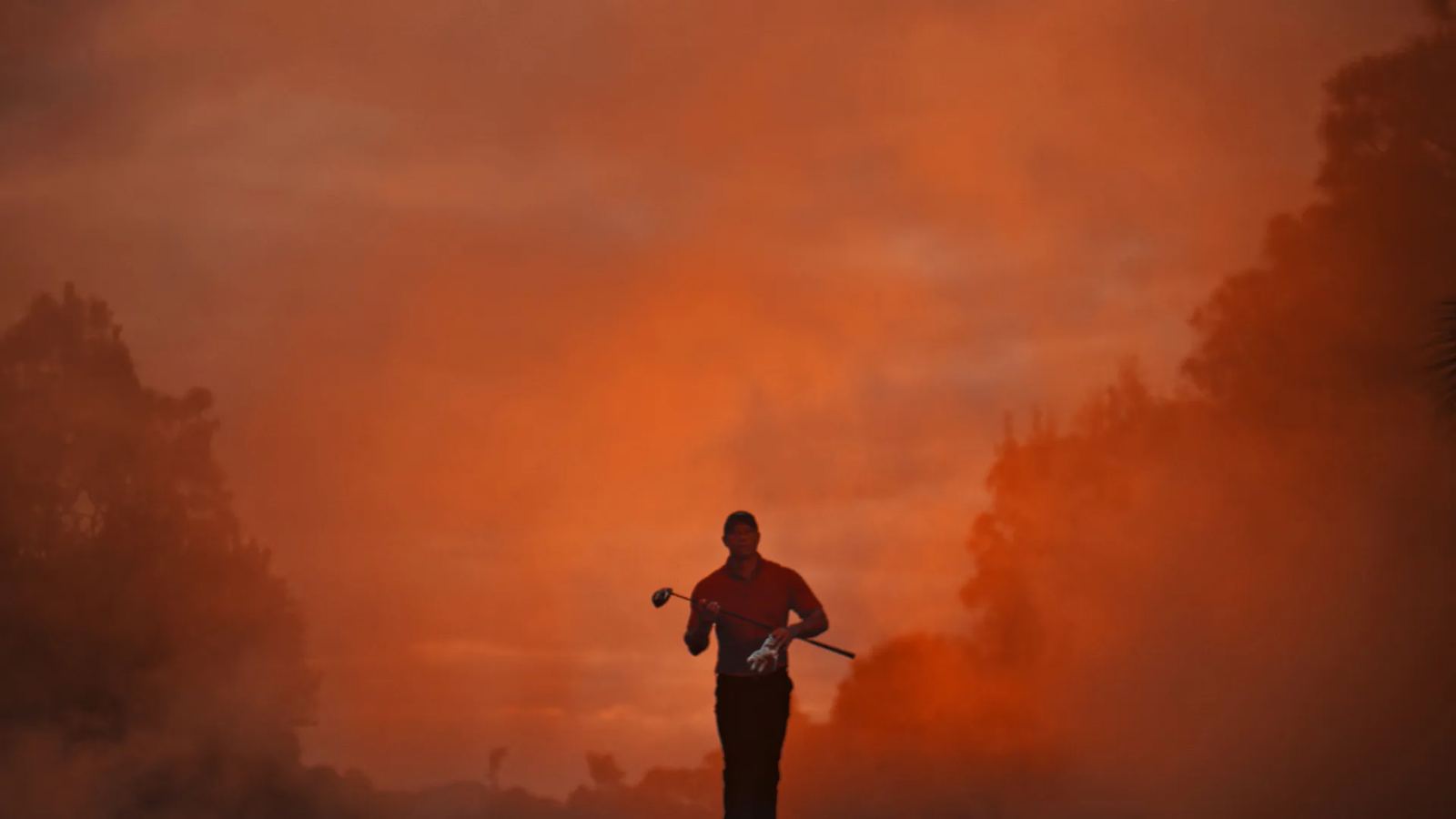 A golfer walks out of red smoke at dawn